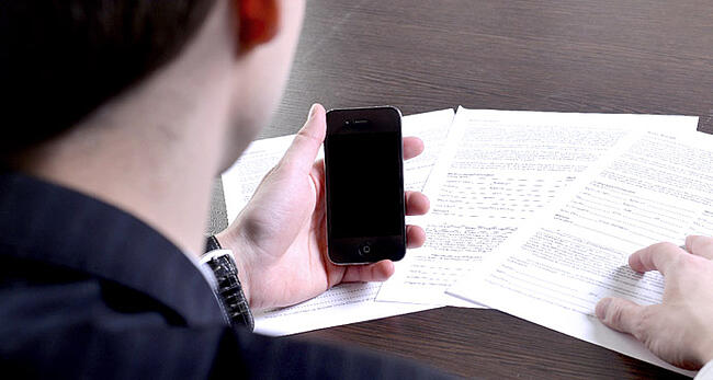 資料を前にスマートフォンを使用する男性の様子