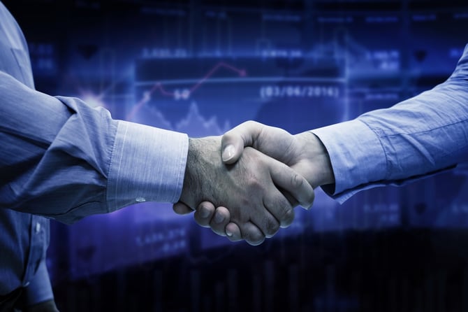 Men shaking hands against stocks and shares.jpeg